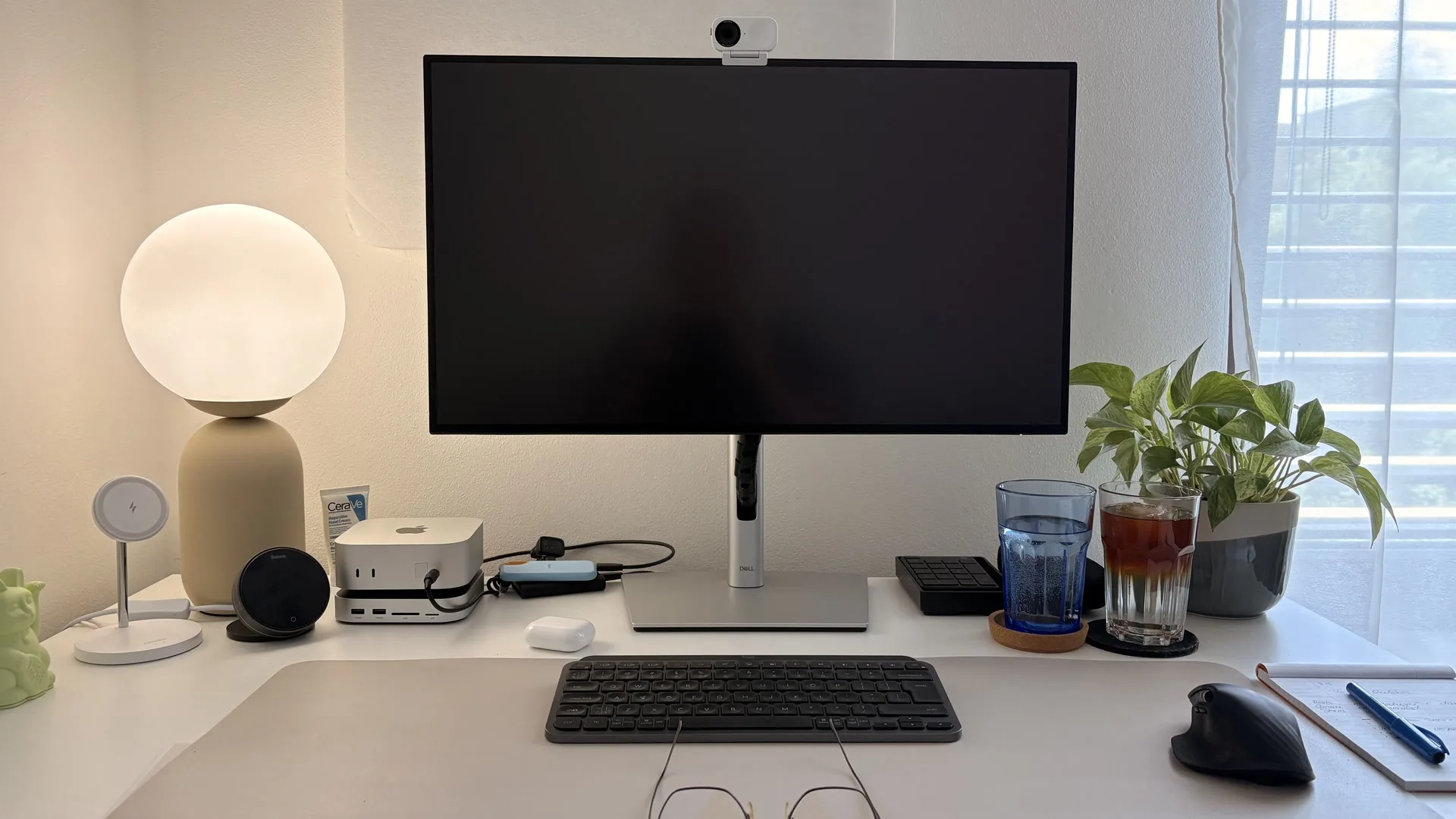 Uklizený pracovní stůl s monitorem, lampou a oknem se záclonou